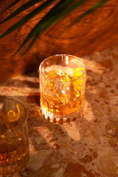 Finished old fashioned cocktail with ice and orange twist, set on a marble bar top in warm lighting