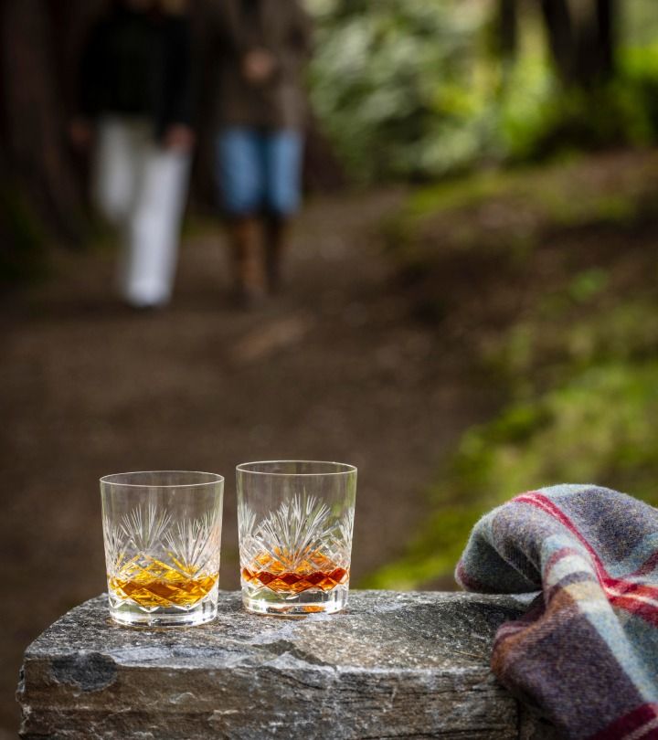 Two whisky glasses on a rustic stone post, with a soft-focus backdrop of a garden.