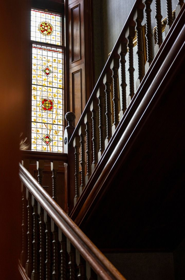 An elegant mahogany staircase with light streaming in through a stained glass window.