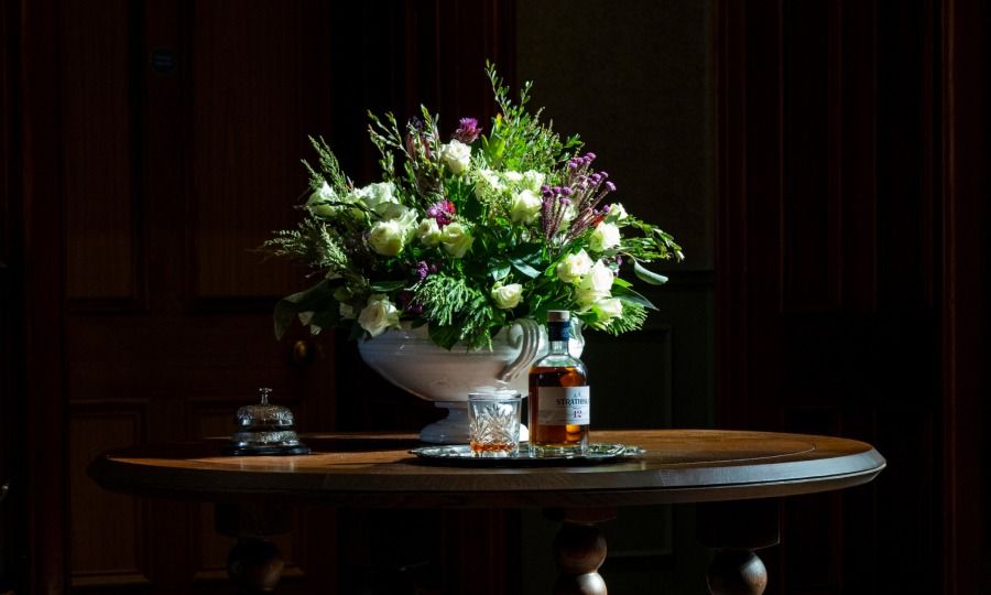 Image of a vase of flowers on an elegant mahogany table with a whisky bottle and glass.