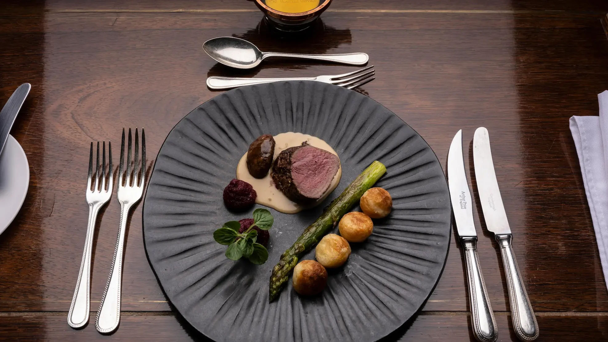Beautifully presented plate of gourmet meat and vegetables on a mahogany table.