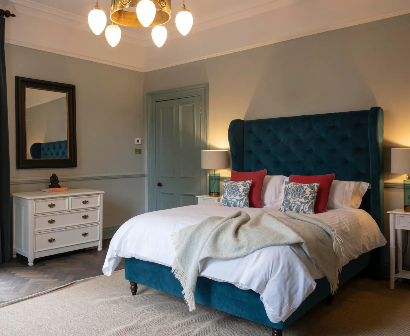 Bright Aberlour bedroom with a large teal bed, white linens, patterned throw pillows and a large bay window.