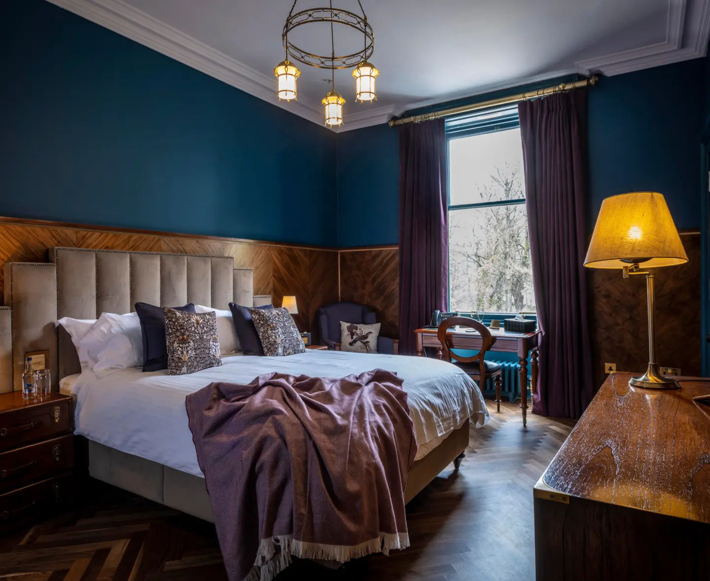 Cozy Longmorn bedroom with a king-size bed, elegant dark teal walls and large windows letting in natural light.