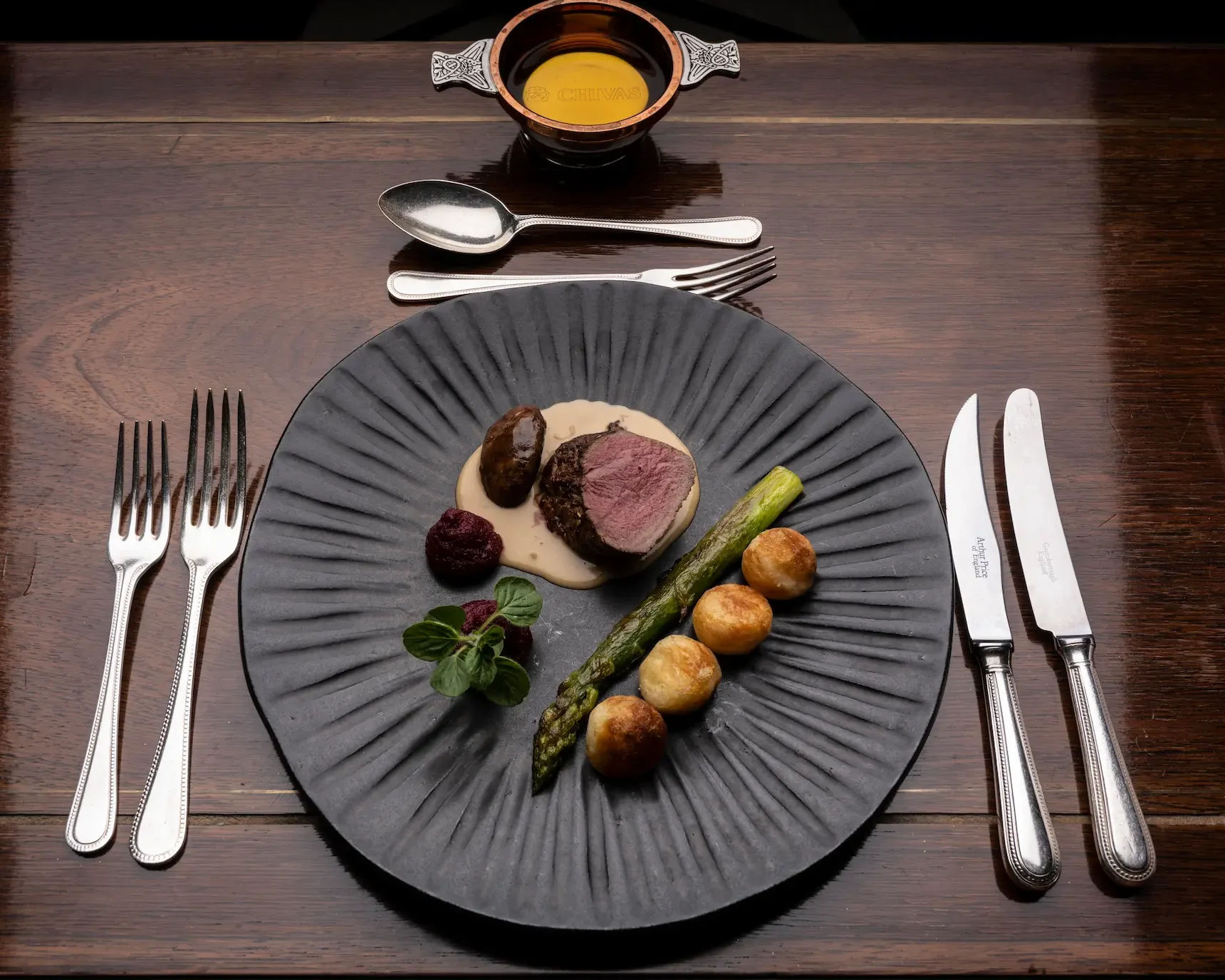 Beautifully presented black plate of gourmet meat and vegetables on a mahogany table.