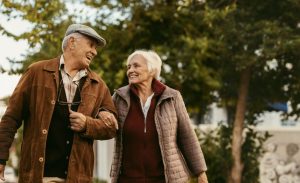 A senior couple shares a smile while out on a walk as they discuss managing care for persons with dementia.