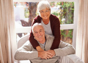 An older woman hugs her husband as they both enjoy the benefits of aging at home.