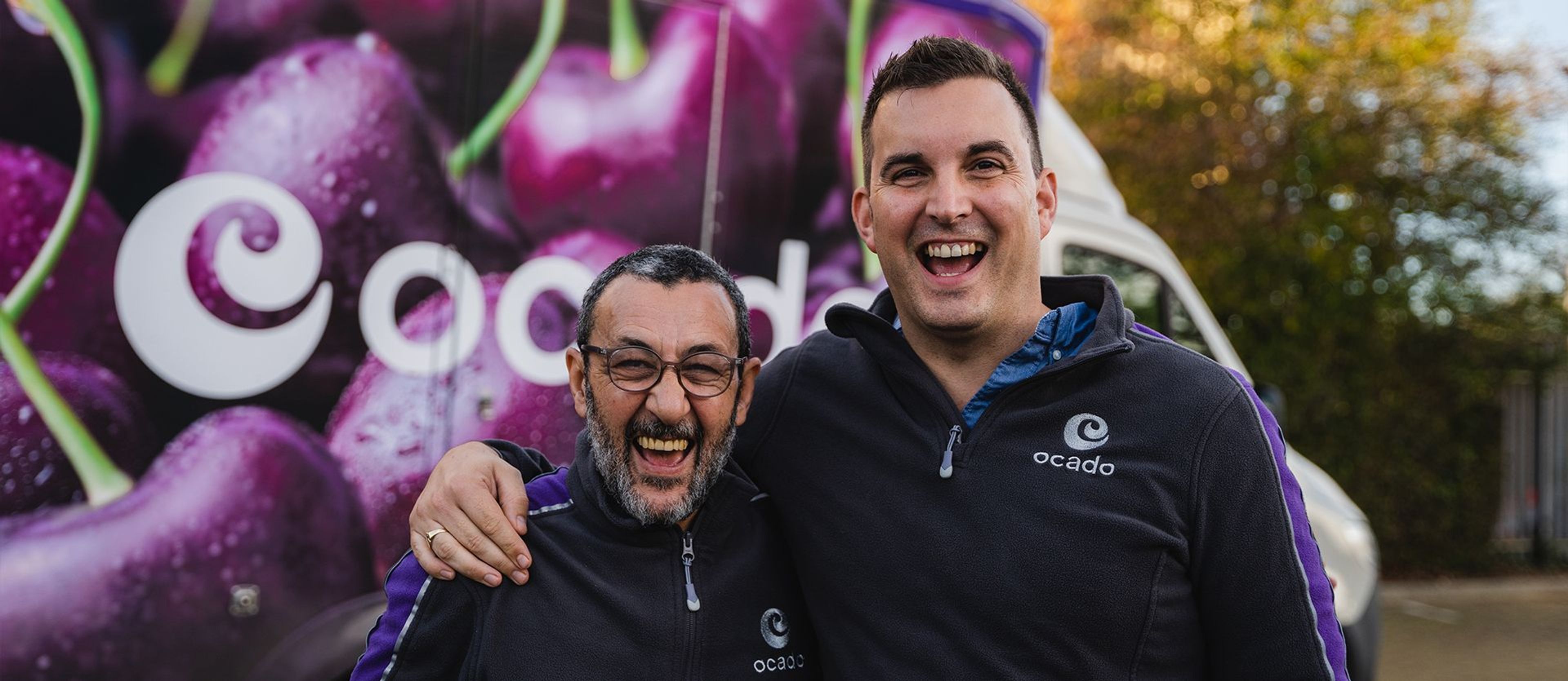 Two Ocado employees in uniform, standing in front of an Ocado van