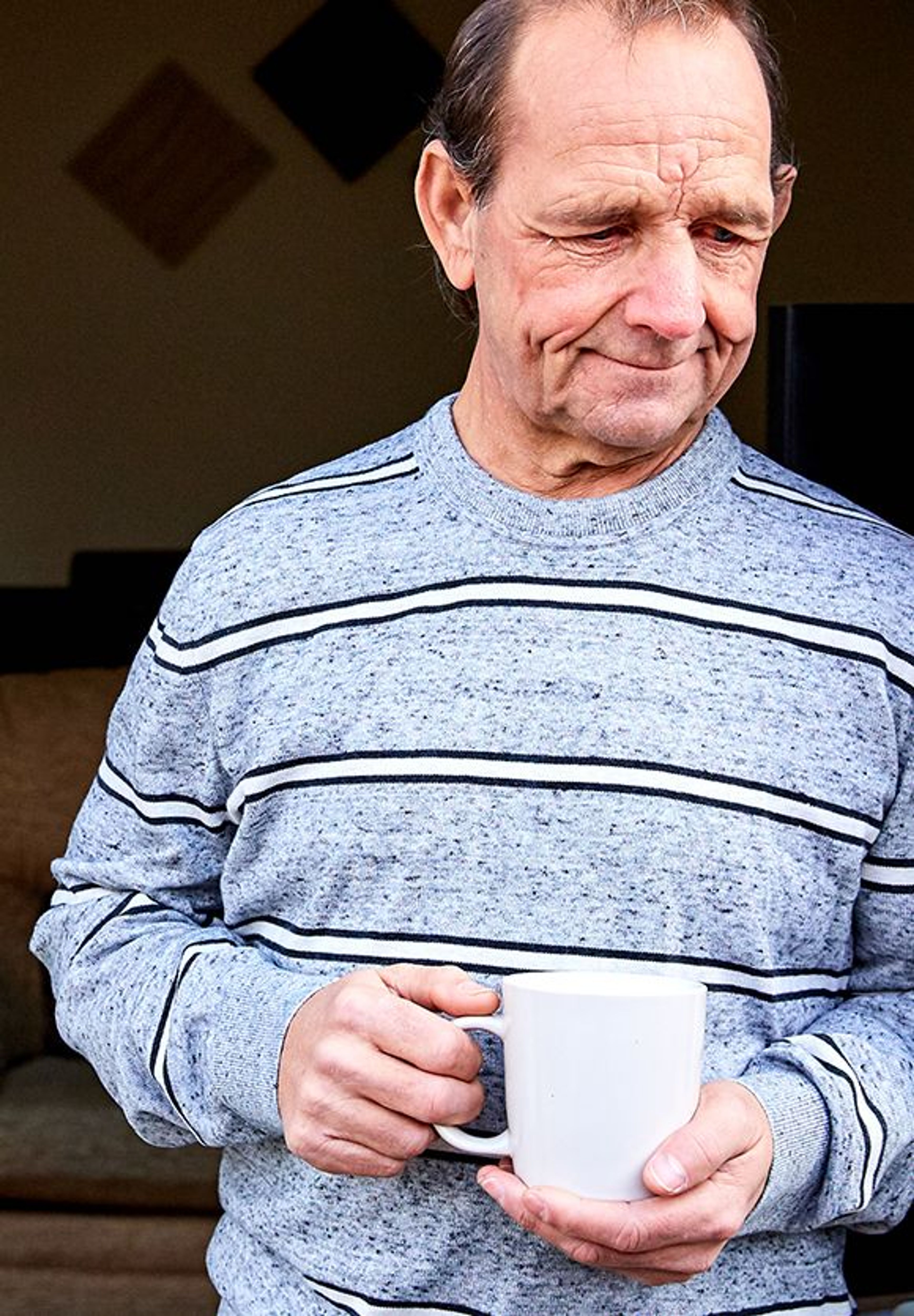 A man with kidney disease leaning against the door frame of his home, with a cup of coffee in his hands, staring at the ground