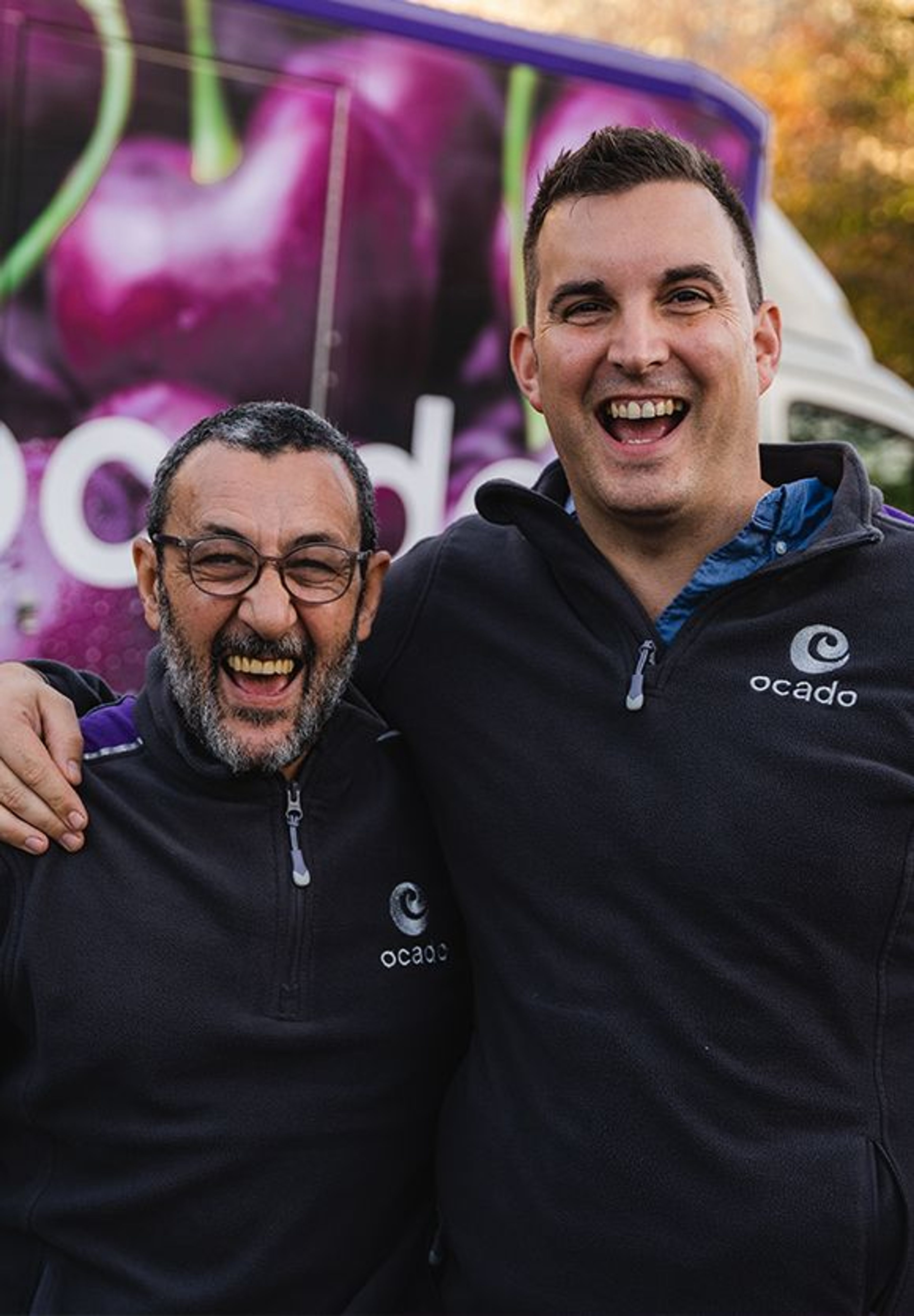 Two Ocado employees in uniform, standing in front of an Ocado van