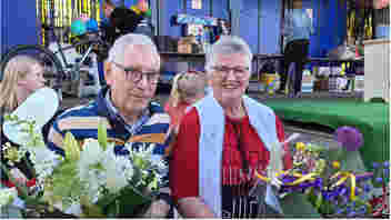 meneer en mevrouw Visser hebben ieder een bos bloemen in de handen, na uitreiking van vergulde hefjes voor hun vrijwilligerswerk de afgelopen 50 jaar voor de rommelmarkt van de kerk