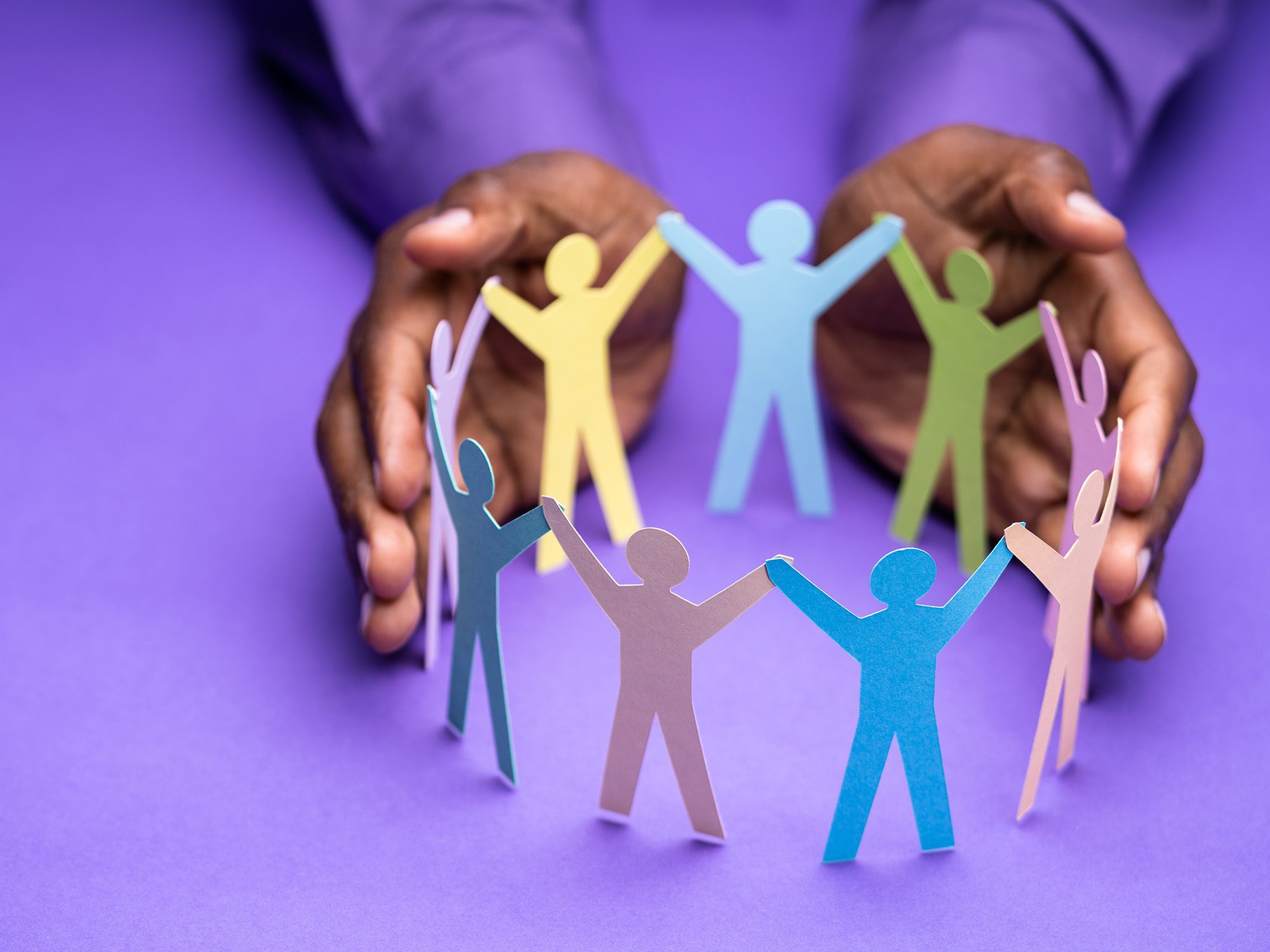 an image of some hands encircing some cut out paper people in a circle