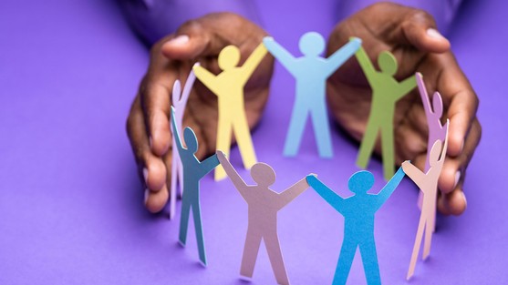 an image of some hands encircing some cut out paper people in a circle