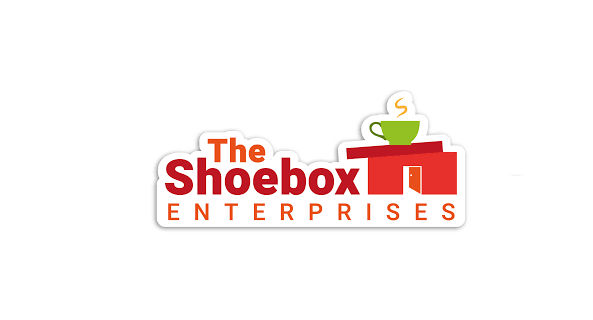 A red shoebox house with a door and a green cup of tea on the top. Next to the words The Shoebox Enterprises in red and orange font