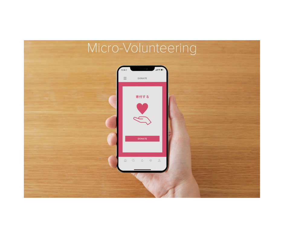 A caucasian right hand holding a smart phone, on the screen there is an icon in read and white of an open palm with a love heart hovering above. The background is the surface of a table.