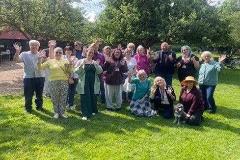 A big group of people in a garden smiling and waving to camera