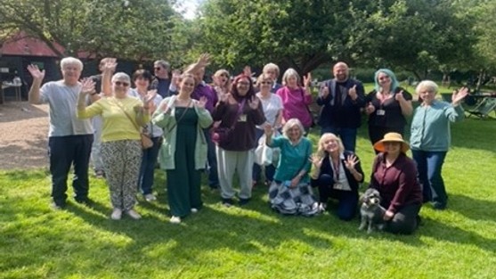 A big group of people in a garden smiling and waving to camera