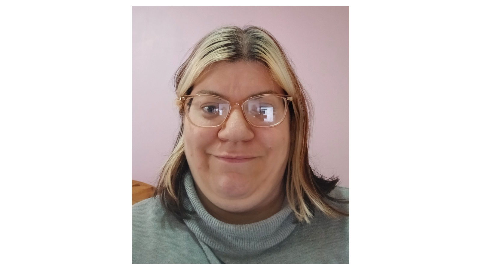 Photo of Kerry, she has shoulder length blonde hair and is smiling to camera. She is wearing a grey polo neck jumper and glasses.