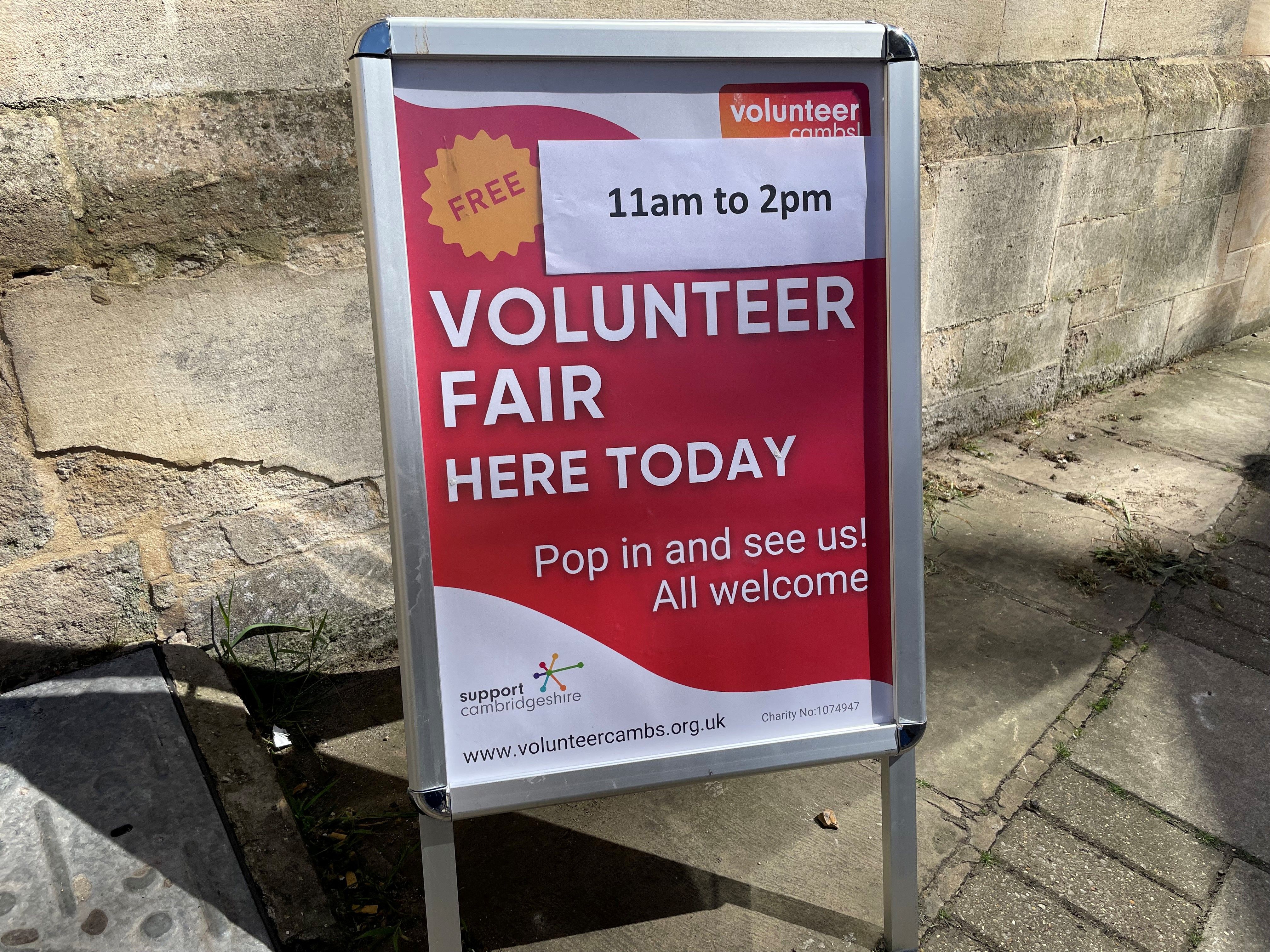 A photo of an A frame displaying a bright red posterfor a Volunteer Fair.
