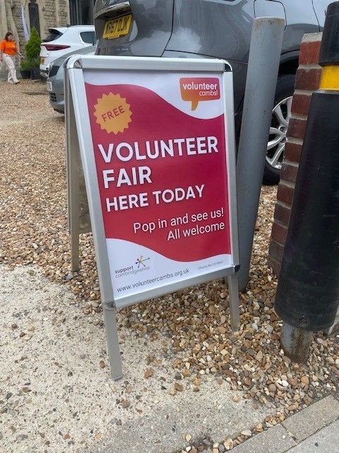 A photo of an A frame displaying a bright red posterfor a Volunteer Fair.