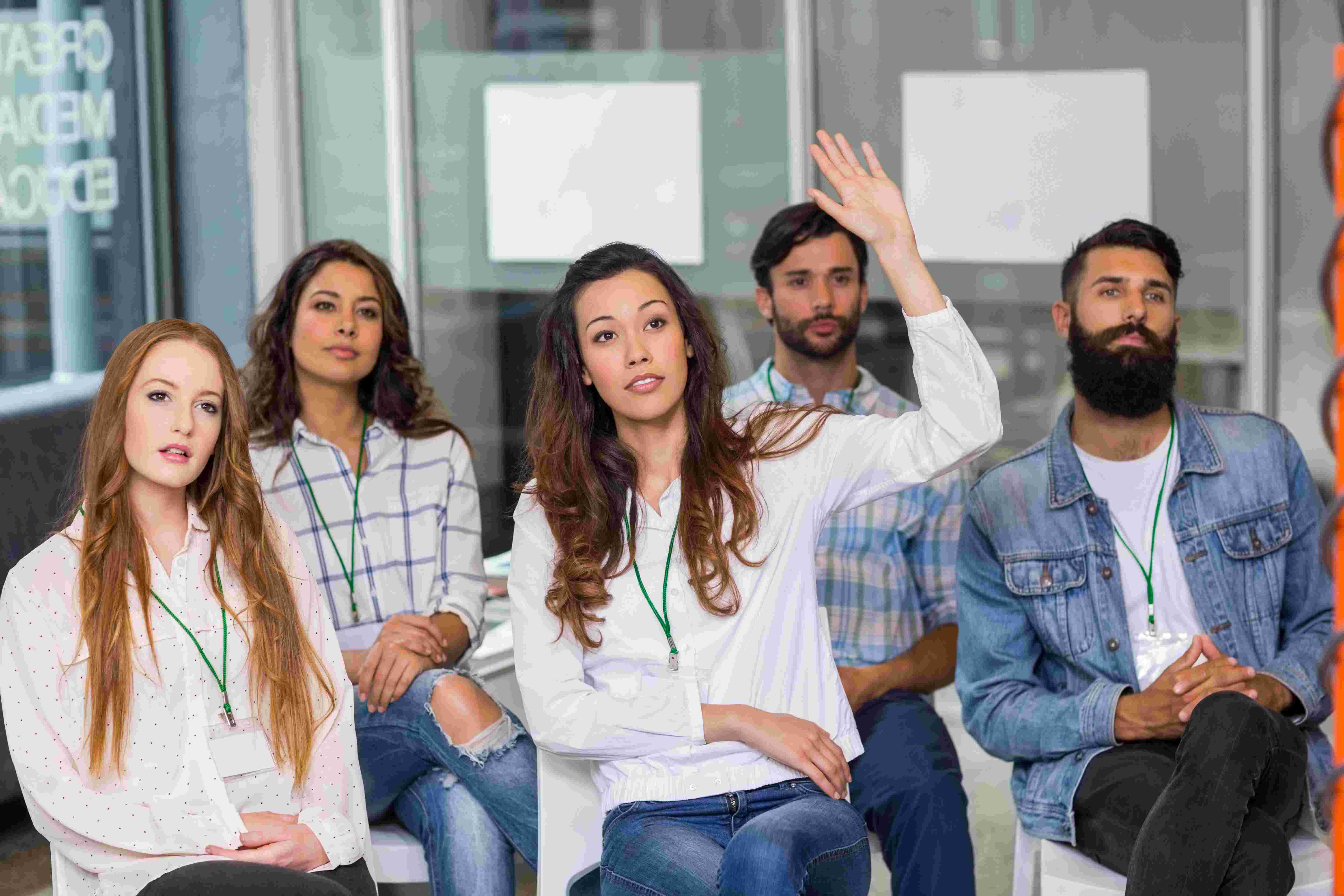 Een groepje mensen waarvan 1 iemand zijn hand opsteekt