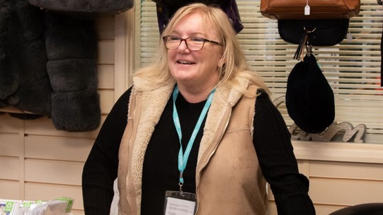Ruth, blonde haired lady with glasses stands at the customer counter in Isabel Hospice shop