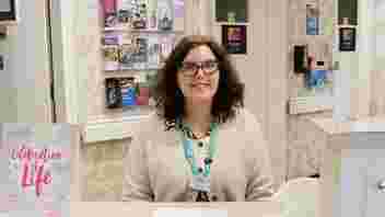 Jenny Burrows has shoulder length brown hair and wears glasses, she smiles at the camera for this photo