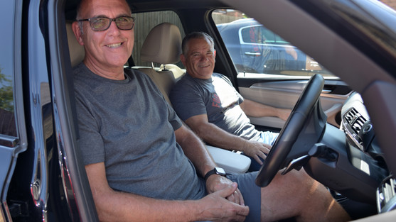 Two gentlemen sitting in a car at the front. Phot taken from the door of the driver.