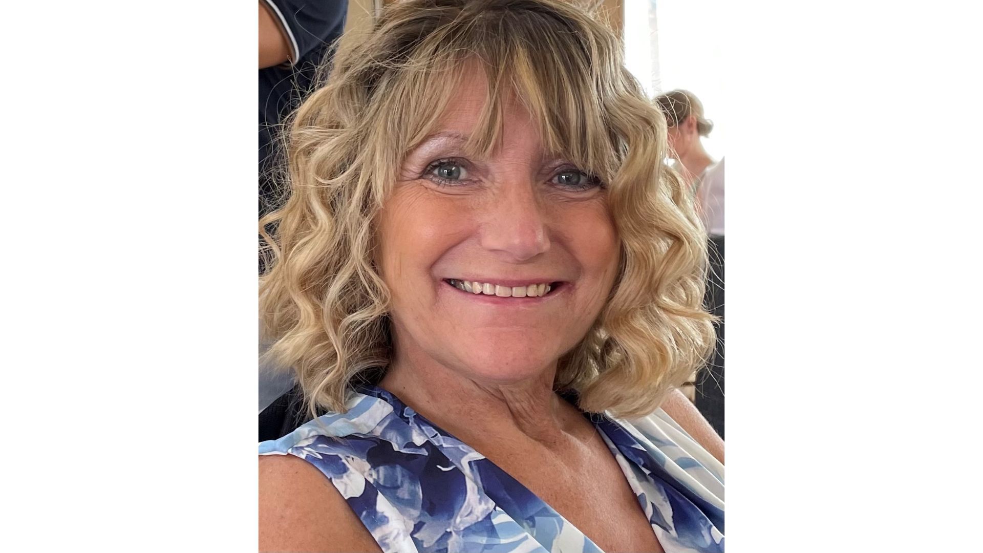 A head and shoulders photo of Kim. She is smiling and is wearing a blue and white top. She has wavy blonde hair and blue eyes.