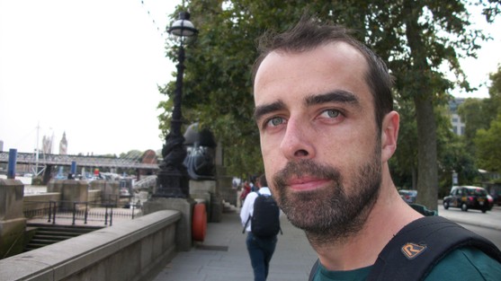 A volunteer is smiling to camera. They have dark hair and a short dark beard.
