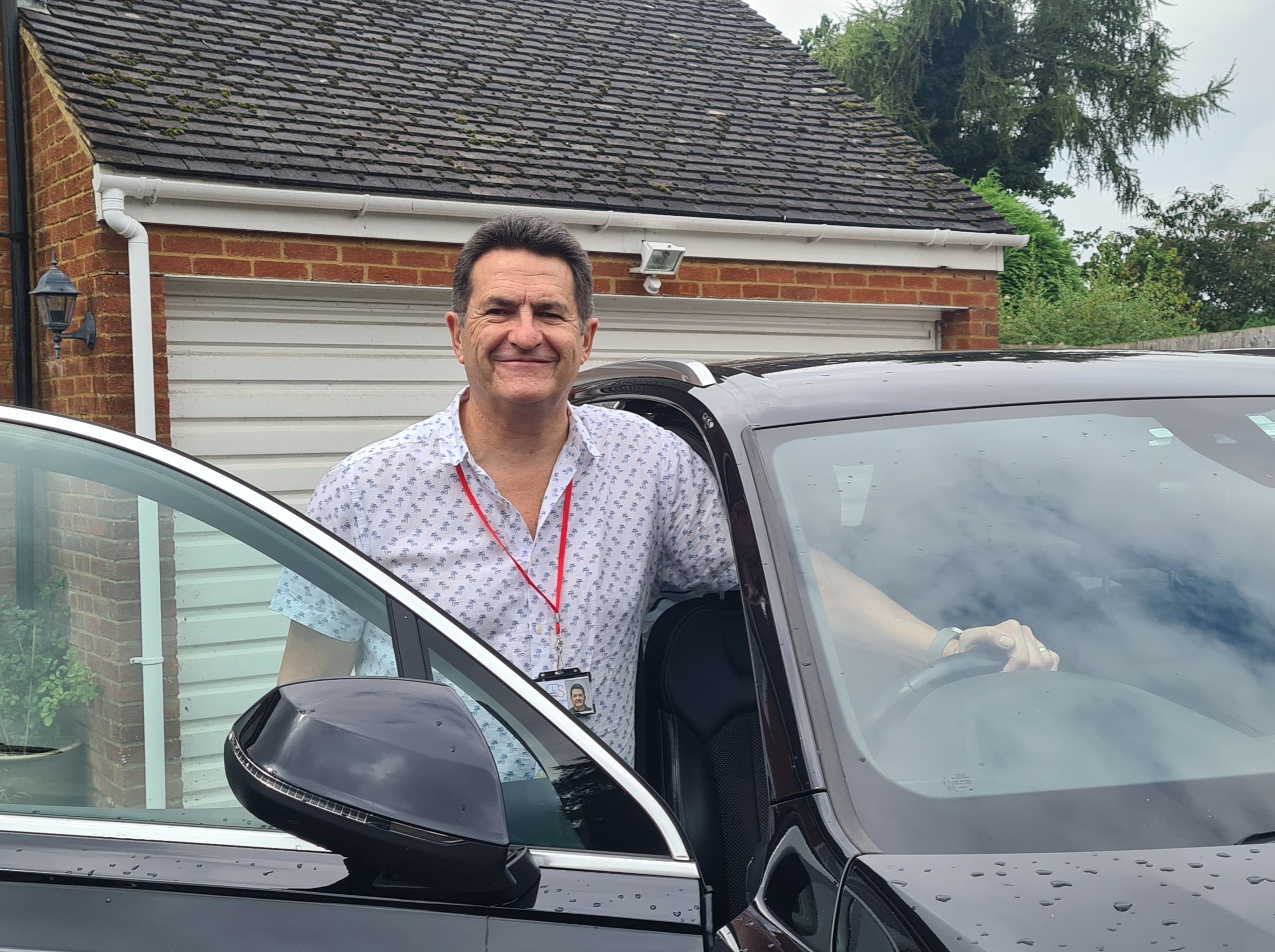 Man standing in a car door way, with one hand on wheel. 