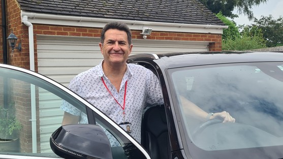 Man standing in a car door way, with one hand on wheel.