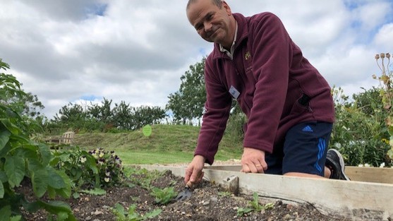 Man on knees holding a small trowel and weeding a flower bed