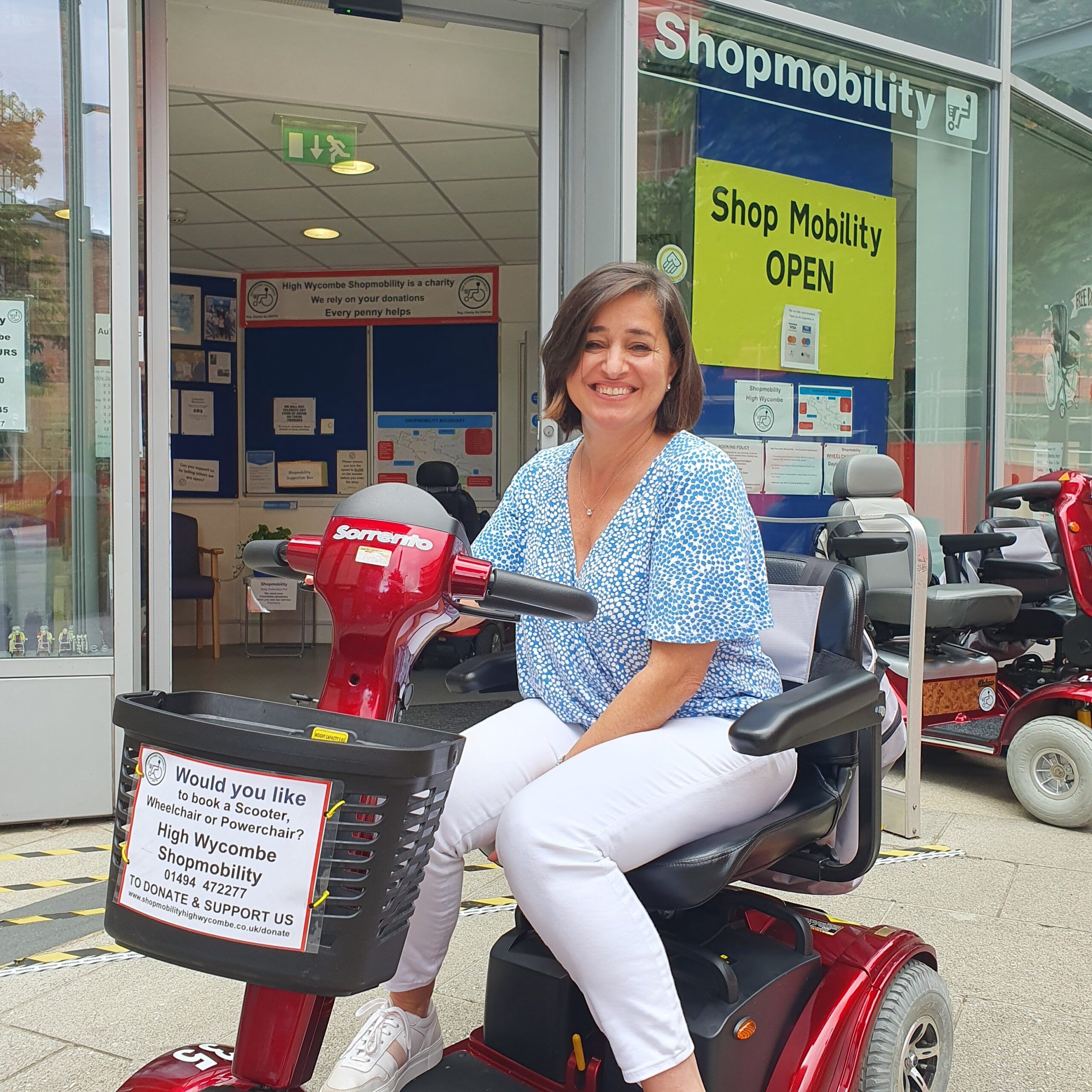 Woman in blue patterned top and white trousers sitting on a mobility scooter