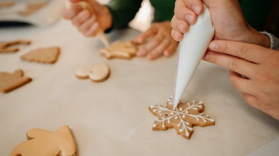 Two pairs of hands holding piping bags, decorating various shaped biscuits with white icing