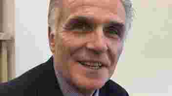 Man who is smiling with white hair, shirt and blue jacket