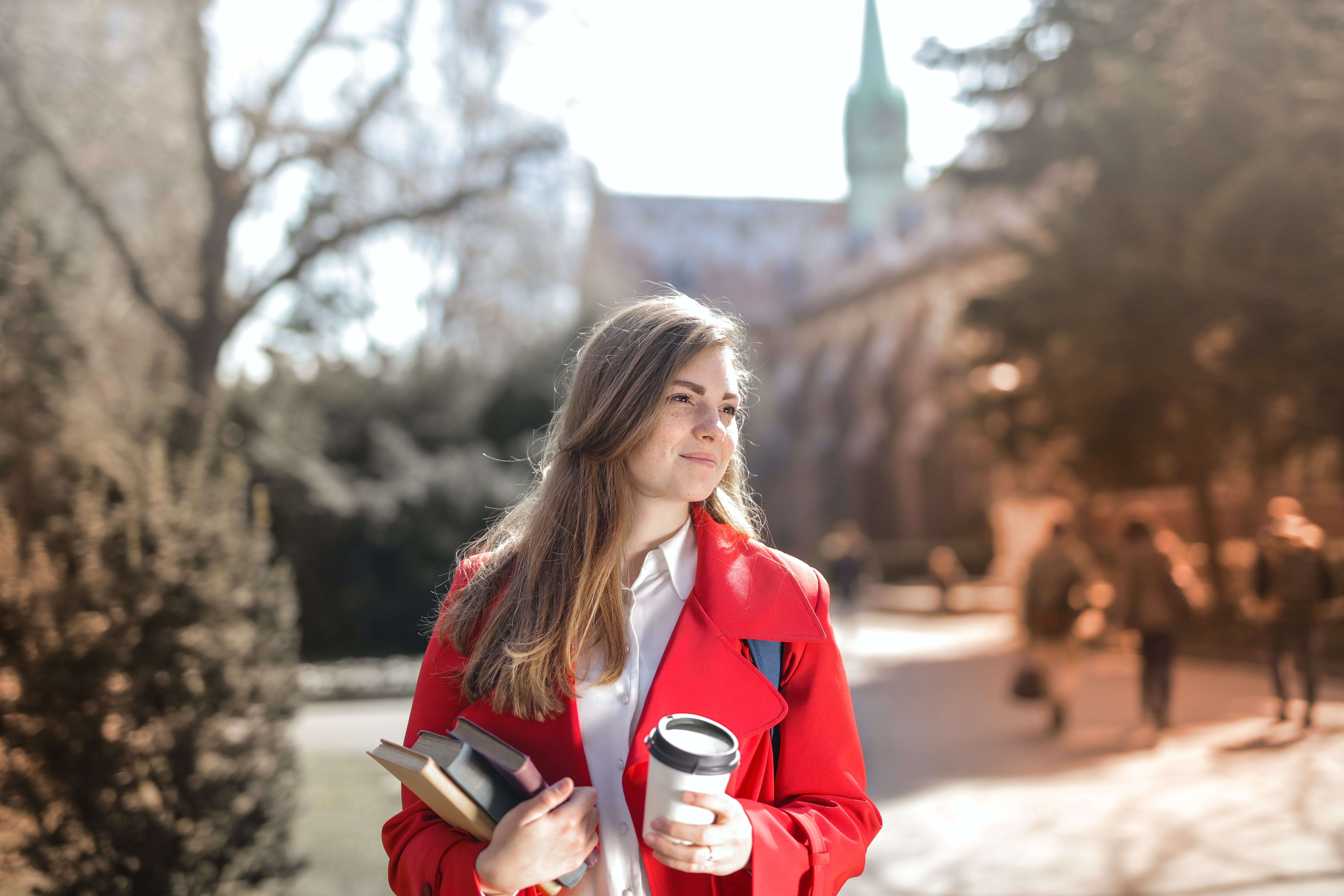 Vrouw met koffie en boeken loopt over straat in de zon