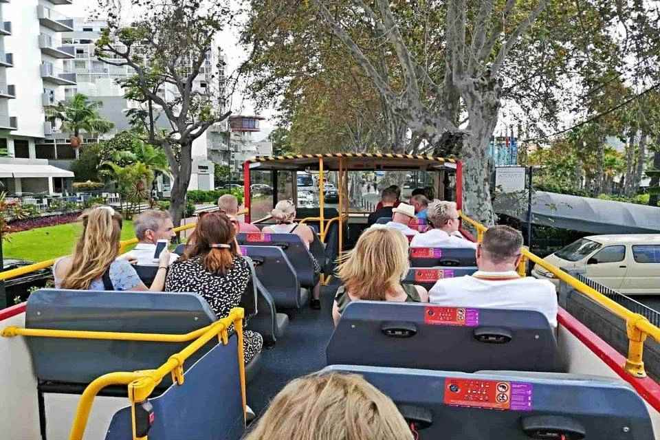  passengers seated on the upper open-air deck of a hop-on hop-off sightseeing double-decker bus