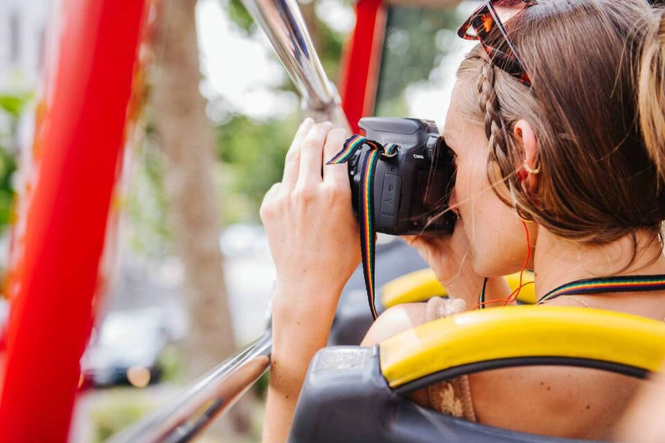 person taking a photo with a digital camera from the upper deck of an open-top sightseeing bus