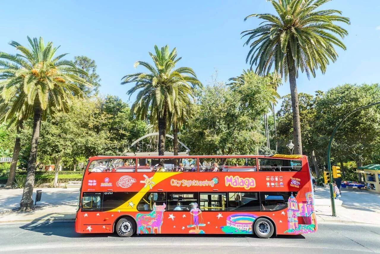 City Sightseeing Hop-on Hop-off bus driving past palm trees in Málaga, Spain