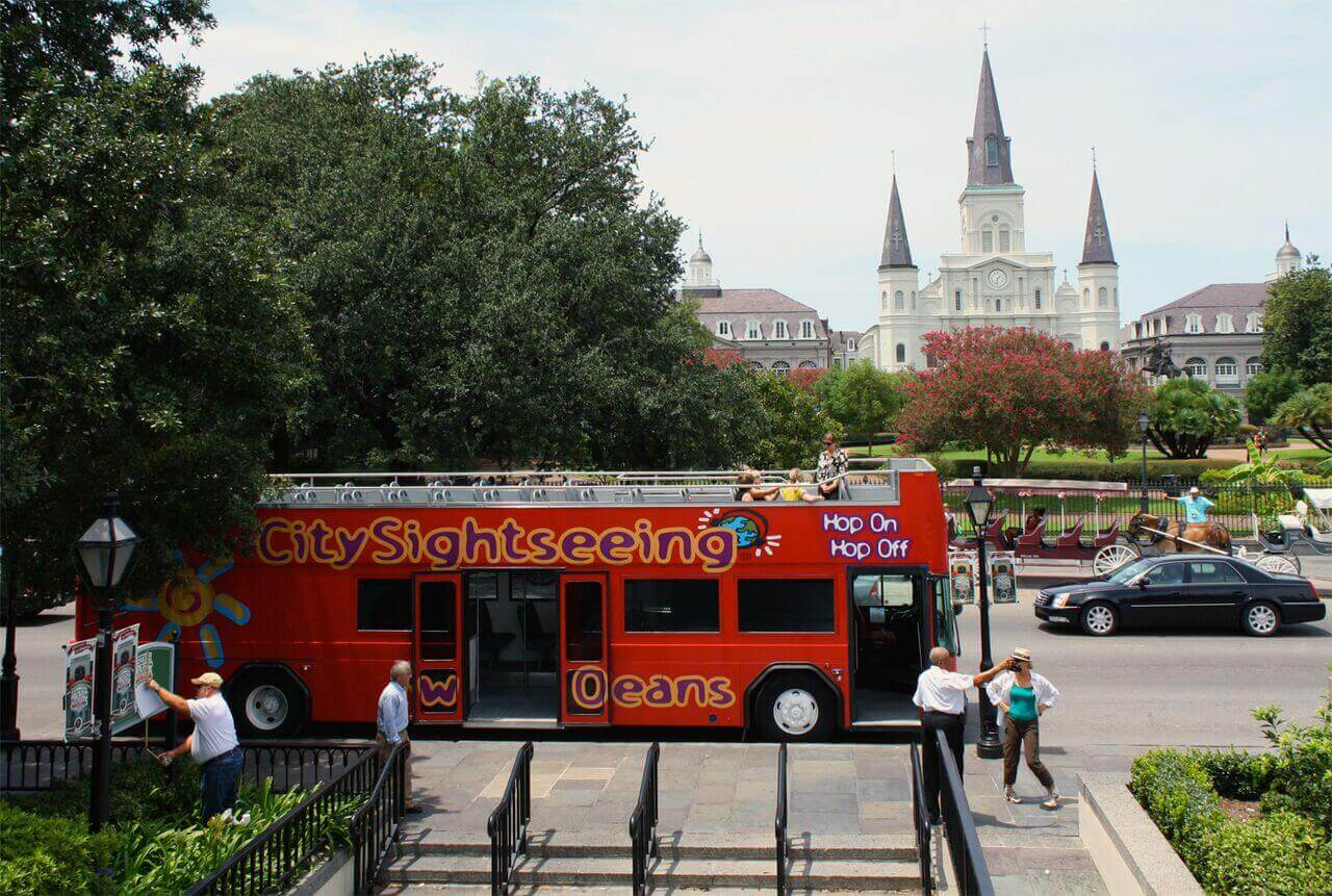 City Sightseeing hop-on, hop-off open-top double-decker bus parked near Jackson Square with the historic St. Louis Cathedral rising in the background in New Orleans