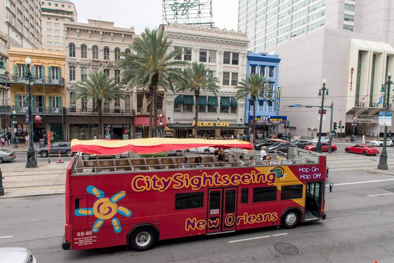 City sightseeing open-top double-decker hop-on hop-off tour bus  driving along Canal Street in New Orleans, Louisiana, passing historic landmarks like the Palace Cafe