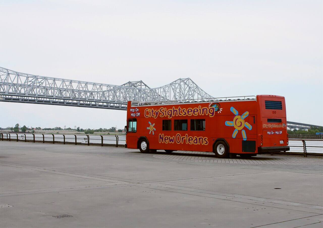 City Sightseeing hop-on hop-off tour bus parked along the New Orleans riverfront near the iconic Crescent City Connection bridge