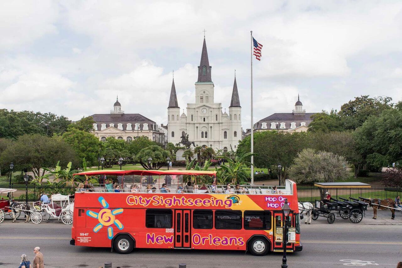 City Sightseeing double-decker open-top tour bus driving past Jackson Square in front of the historic St. Louis Cathedral in New Orleans, Louisiana
