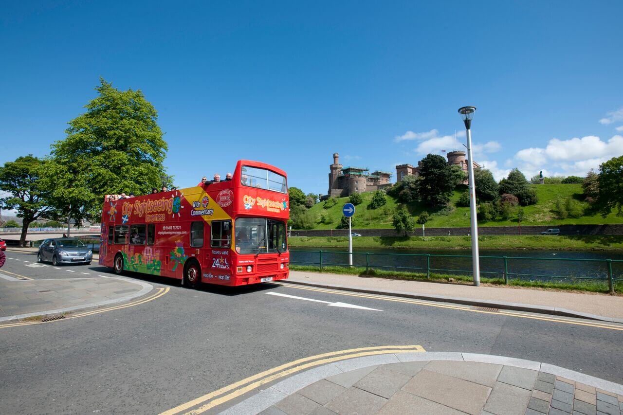 City Sightseeing Inverness Hop-On Hop-Off Bus Tour operating near the River Ness with Inverness Castle