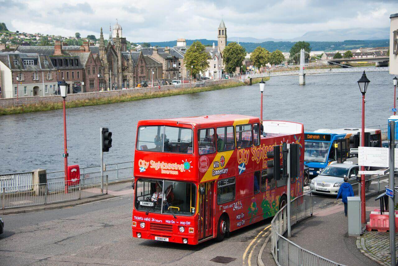 City Sightseeing open-top double-decker bus on a hop-on hop-off tour driving along the River Ness in Inverness