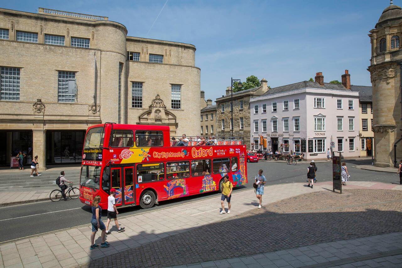 City Sightseeing double-decker open-top tour bus operating on a hop-on, hop-off route through the historic streets of Oxford, England