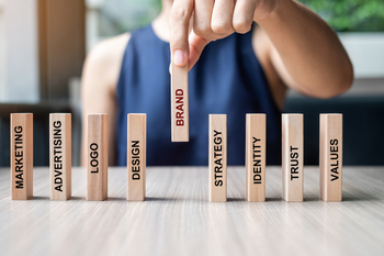 Businesswoman hand placing or pulling wooden Dominoes with BRAND text