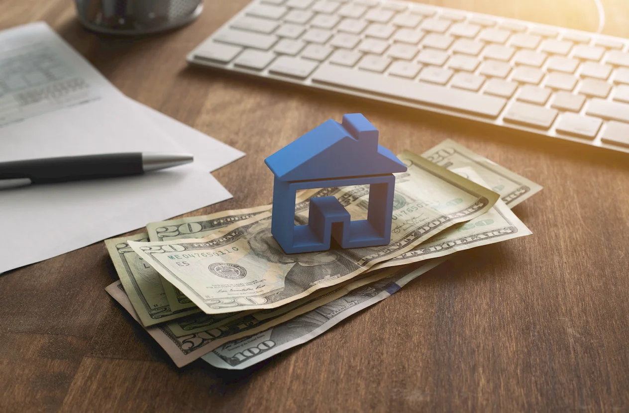 3d-house-on-pile-of-money-with-tax-and-financial-forms-on-the-desk.webp