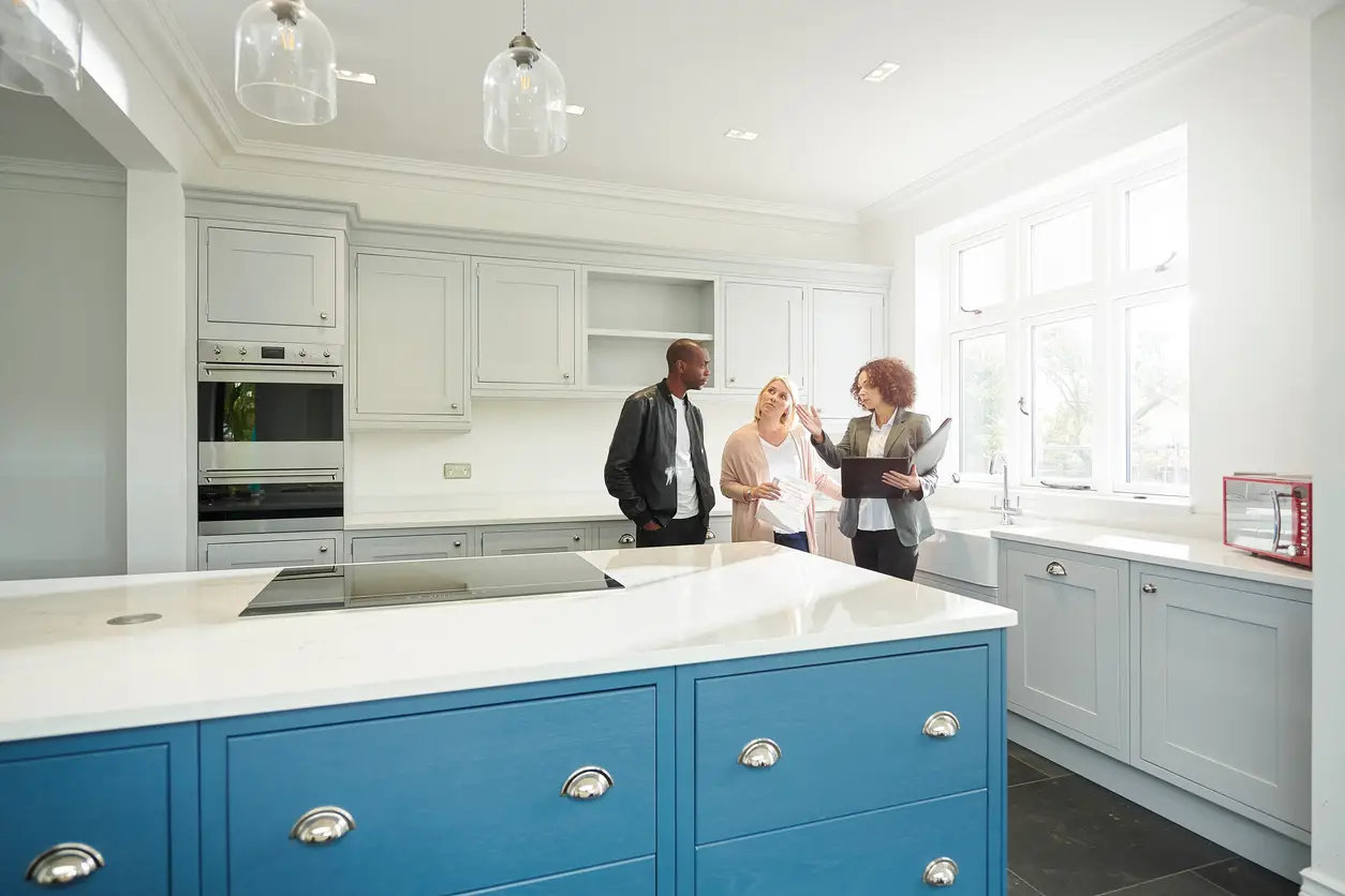 a-saleswoman-or-estate-agent-shows-a-couple-around-a-home-with-new-kitchen.webp