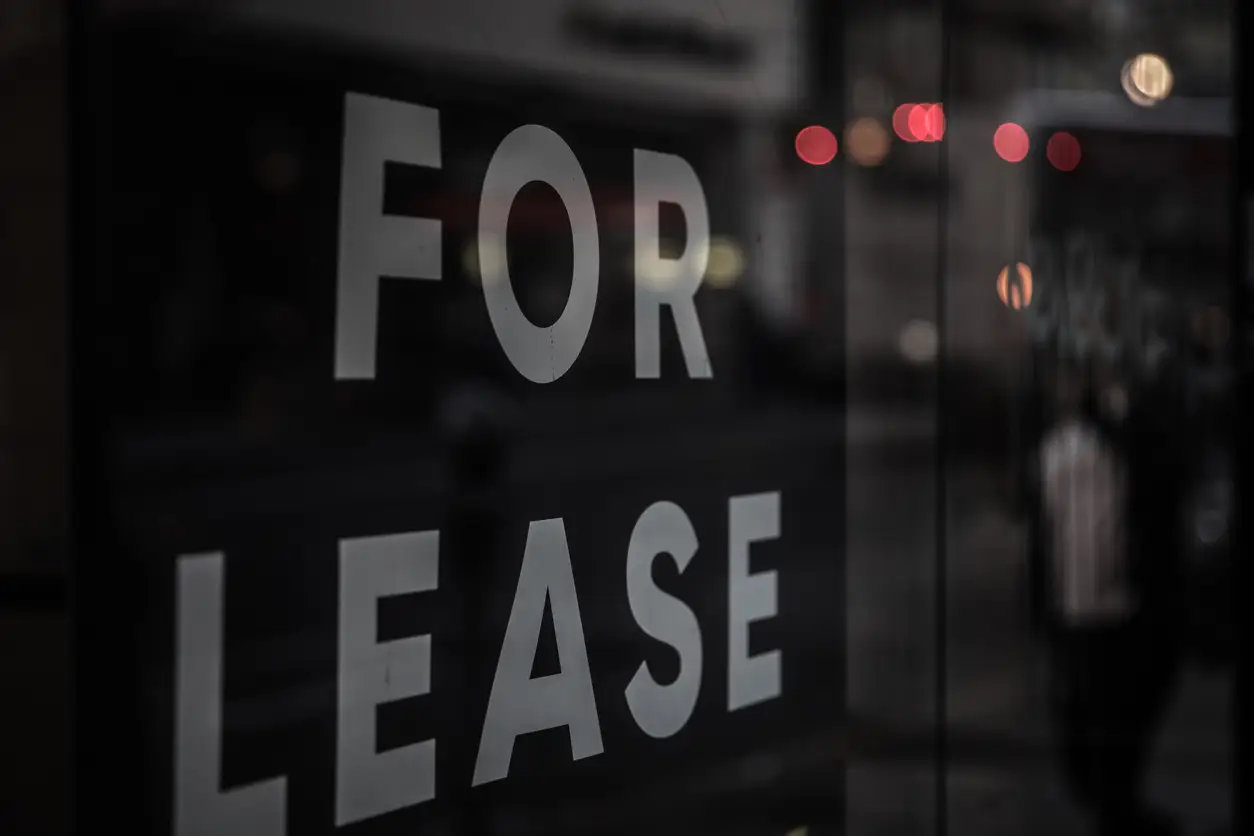 for-lease-sign-in-vacant-storefront-window-with-a-reflection-of-city-lights-and-bus-in-the-window-retail-struggle.webp